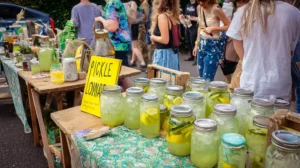 Outdoor fair stand selling Pickle Lemonade with bright signage and jars of green lemonade