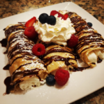Crispy xango dessert with cheesecake filling, caramel and chocolate drizzle, whipped cream, ice cream, and berries on a plate.