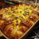 Ham and cheese croissant casserole with golden top in a white baking dish, sliced and ready to serve