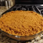 Golden homemade graham cracker crust pressed into a pie pan with crumbs and butter visible