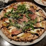 White pizza with prosciutto, arugula, and balsamic glaze on a wooden board
