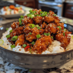 Amateur phone photo of crispy General Tso’s Chicken coated in glossy sweet-and-spicy sauce, served over a big pile of white rice with green onions.
