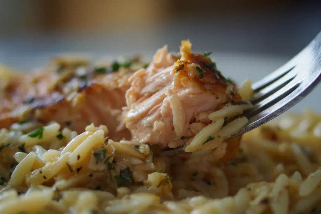 Fork flaking salmon to check doneness over creamy orzo