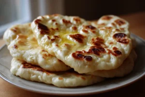 Stack of homemade 2 ingredient naan bread on a plate with golden bubbles and light char spots