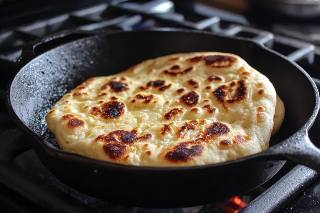 Naan bread cooking in a cast iron skillet with bubbles forming on the surface