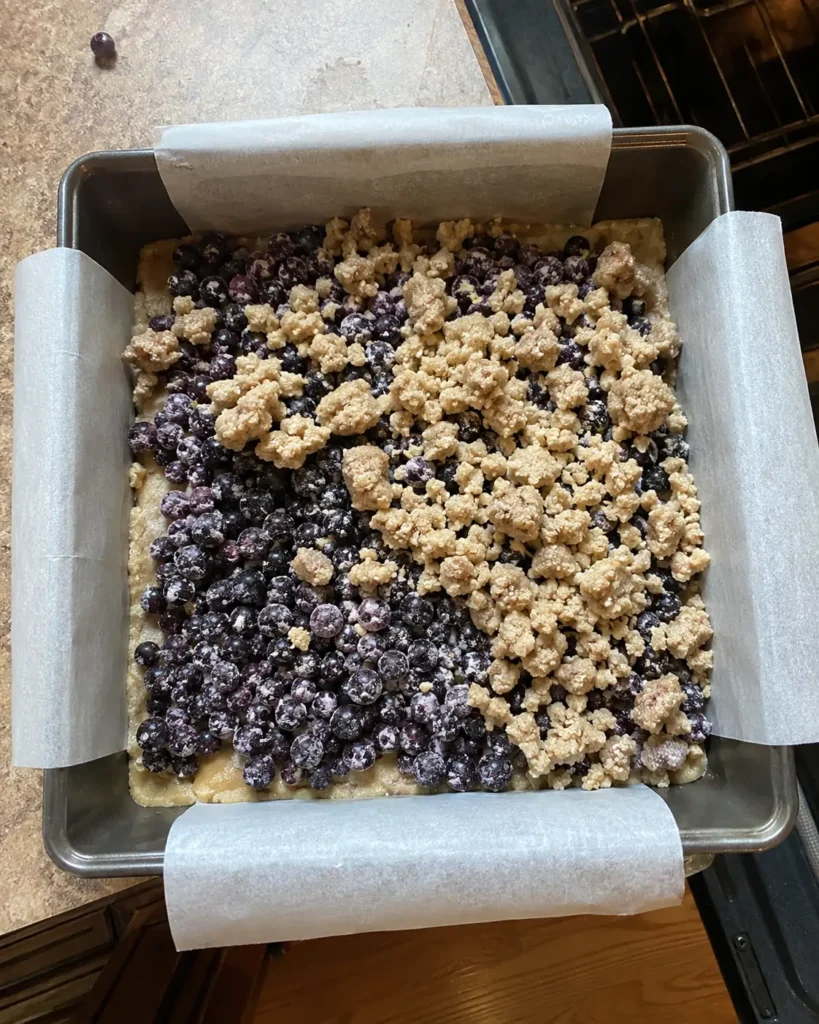 Huckleberries and crumble topping layered over the prebaked crust for Huckleberry Crumb Bars