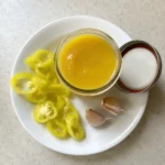 Banana pepper hot sauce in a glass jar with fresh pepper slices and garlic