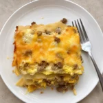 A slice of Breakfast Lasagna on a white plate showing cheesy egg and sausage layers