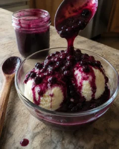 Homemade Huckleberry Sauce spooned over vanilla ice cream in a glass bowl