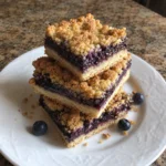 Stack of Huckleberry Crumb Bars on a white plate showing the layered shortbread crust and berry filling
