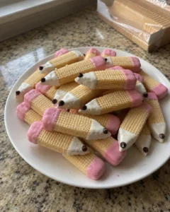 Sugar Wafer Pencil Cookies piled on a white plate with pink candy erasers and white dipped tips