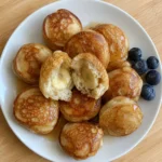 Overhead view of golden Banana Pancake Bites on a plate with one bite broken open