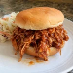 Crockpot BBQ Chicken piled on a bun with coleslaw on the side