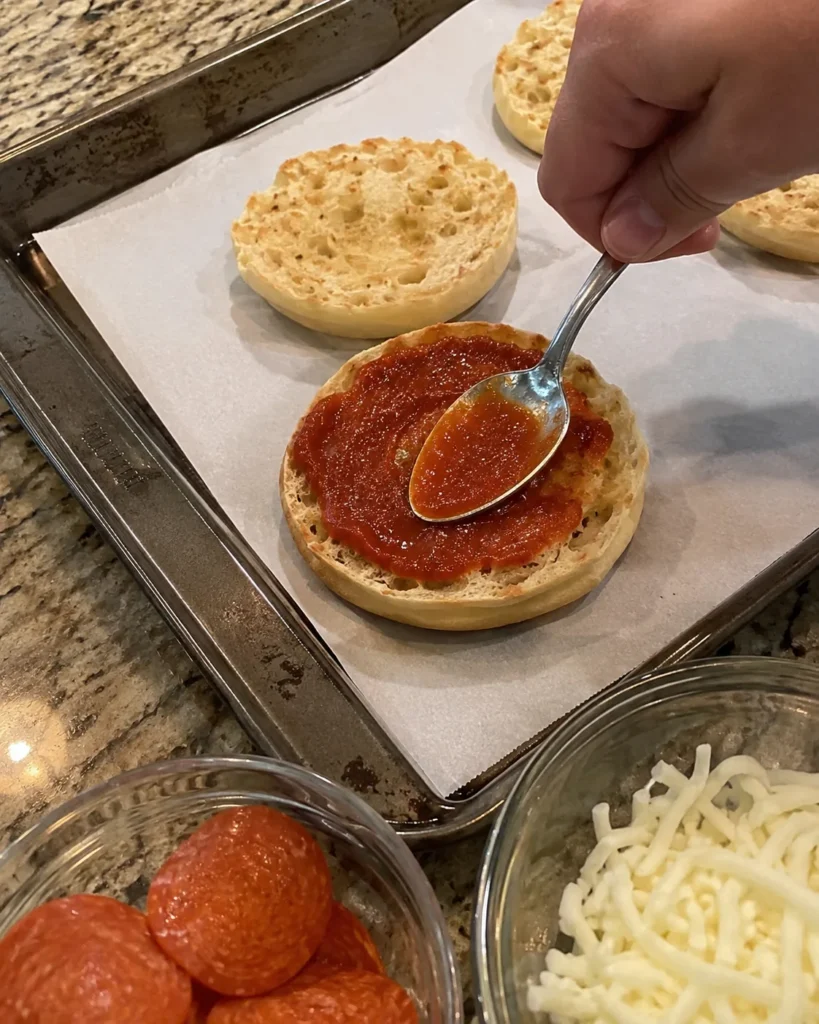 Spreading pizza sauce on a toasted English muffin half