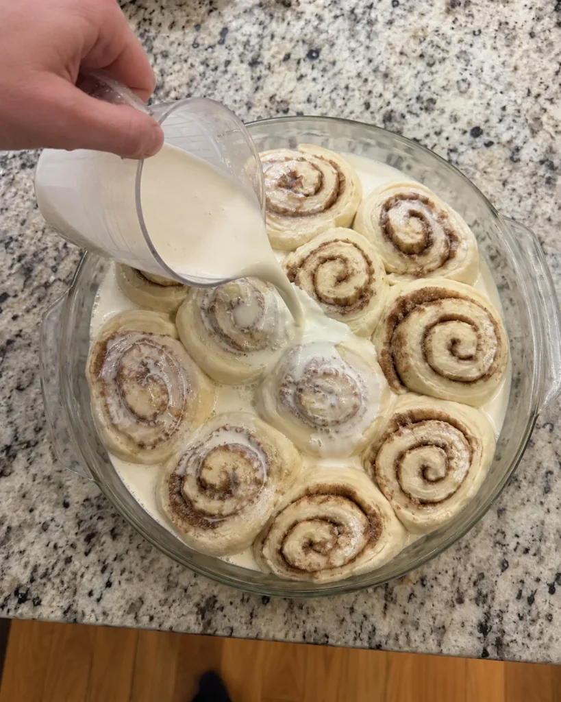 Pouring heavy cream over unbaked cinnamon rolls before baking