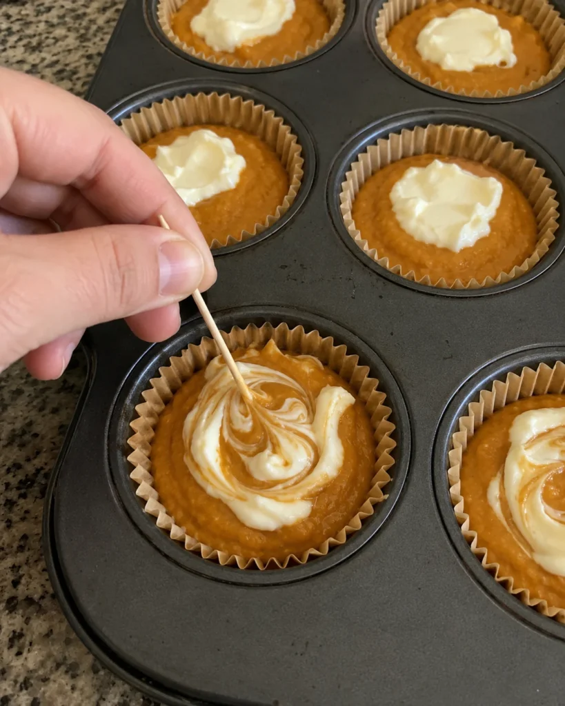 Swirling cream cheese into Pumpkin Cream Cheese Muffins batter with a toothpick