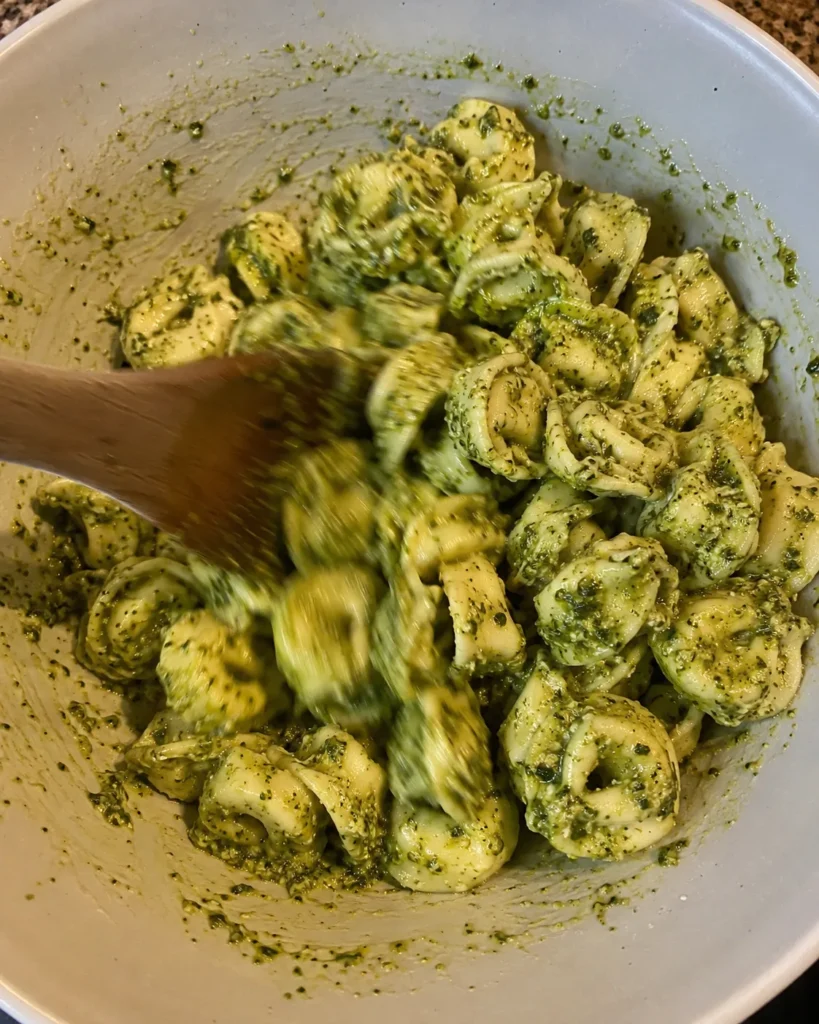 Tossing tortellini with pesto while making Easy Pesto Tortellini Pasta Salad