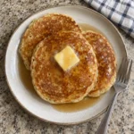Overhead view of golden-brown apple cider pancakes with melting butter and syrup