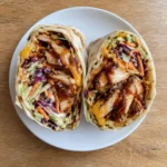 Overhead view of a BBQ chicken wrap with crunchy coleslaw and cheddar on a white plate