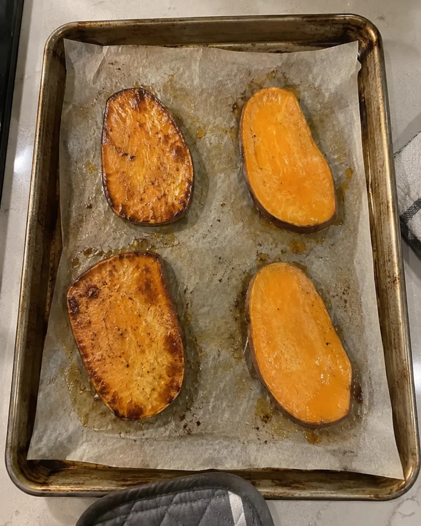 Sweet potato slices on a parchment-lined baking sheet halfway through roasting