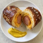 Soft baked cheesy pretzel dog sliced in half showing melted cheddar and hot dog inside