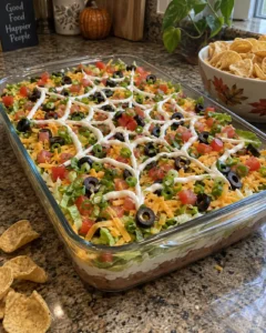 Easy Halloween potluck dishes featuring a spiderweb layered taco dip in a 9x13 dish with tortilla chips