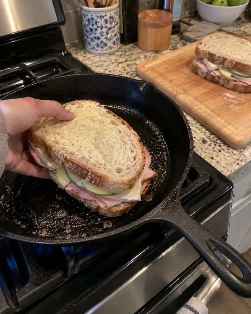 Grilling a ham brie and apple sandwich in a cast-iron skillet over medium heat