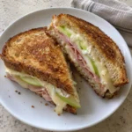 Grilled ham and brie sandwich with apple slices on a white plate