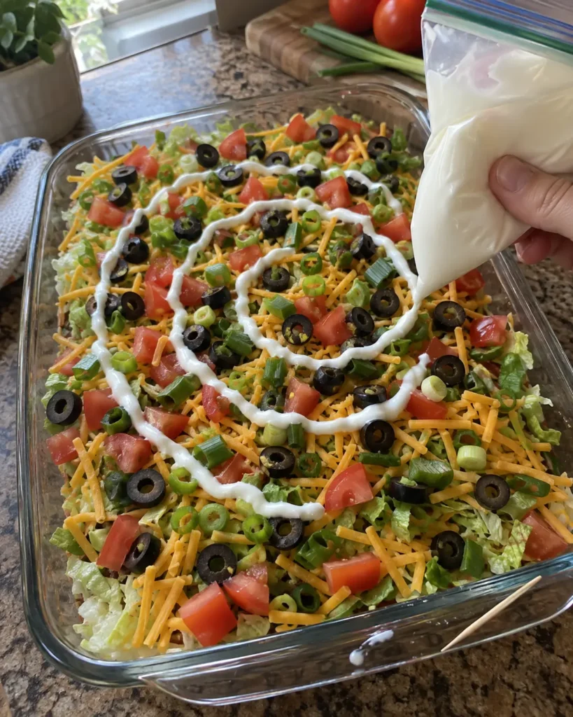 Piping concentric sour cream rings onto layered taco dip before dragging a toothpick outward