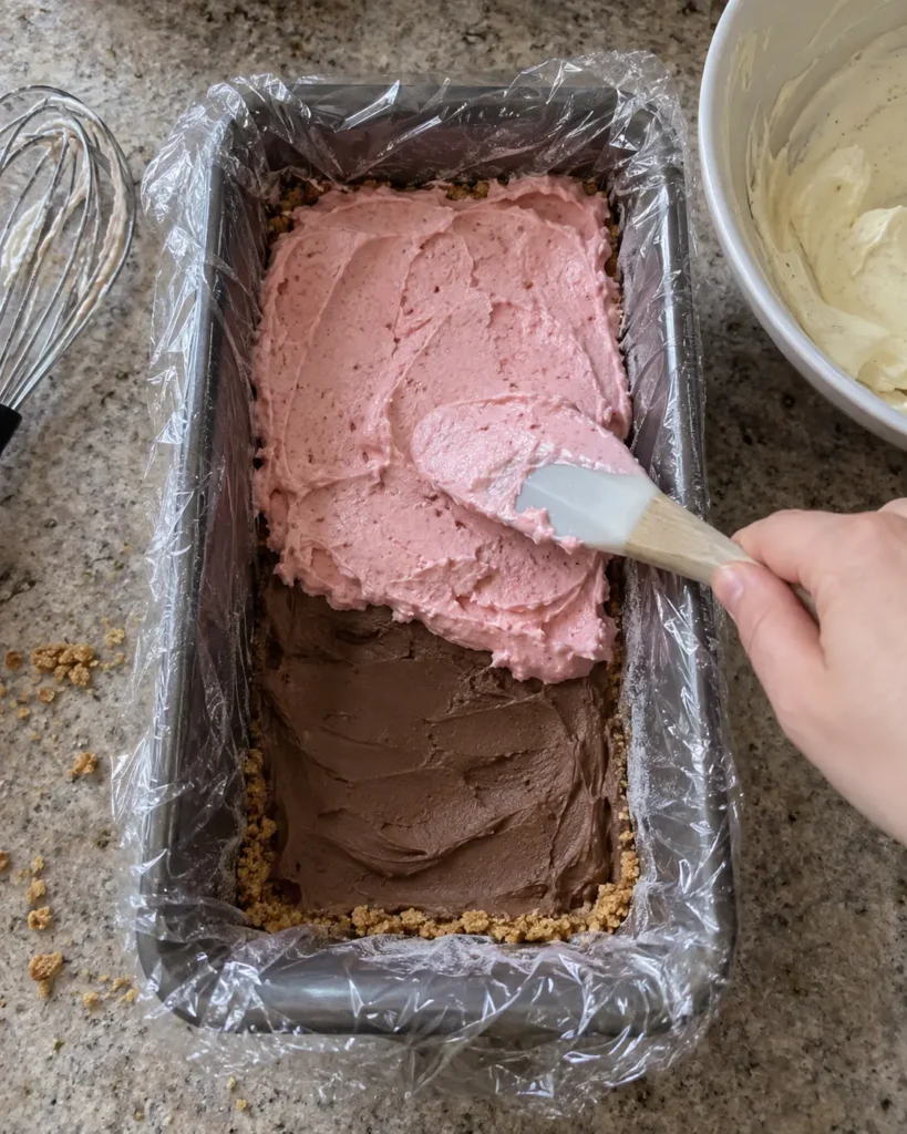 Spreading the strawberry layer over the chocolate layer in a loaf pan to make no-churn Neapolitan ice cream cake