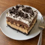 A single slice of layered no-bake chocolate peanut butter Oreo dessert on a white plate