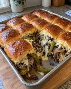Philly cheesesteak slider buns in a baking dish with melted cheese and golden tops