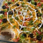 Close view of the sour cream spiderweb on layered taco dip with one scoop removed