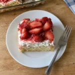 A single strawberry shortcake bar on a white plate showing the cake, frosting, and berry layers