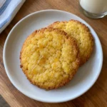 Single sweet cornbread cookie on a white plate showing golden edges and soft center