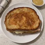 Whole turkey Dijon melt sandwich on a plate with golden buttery sourdough and melted cheese
